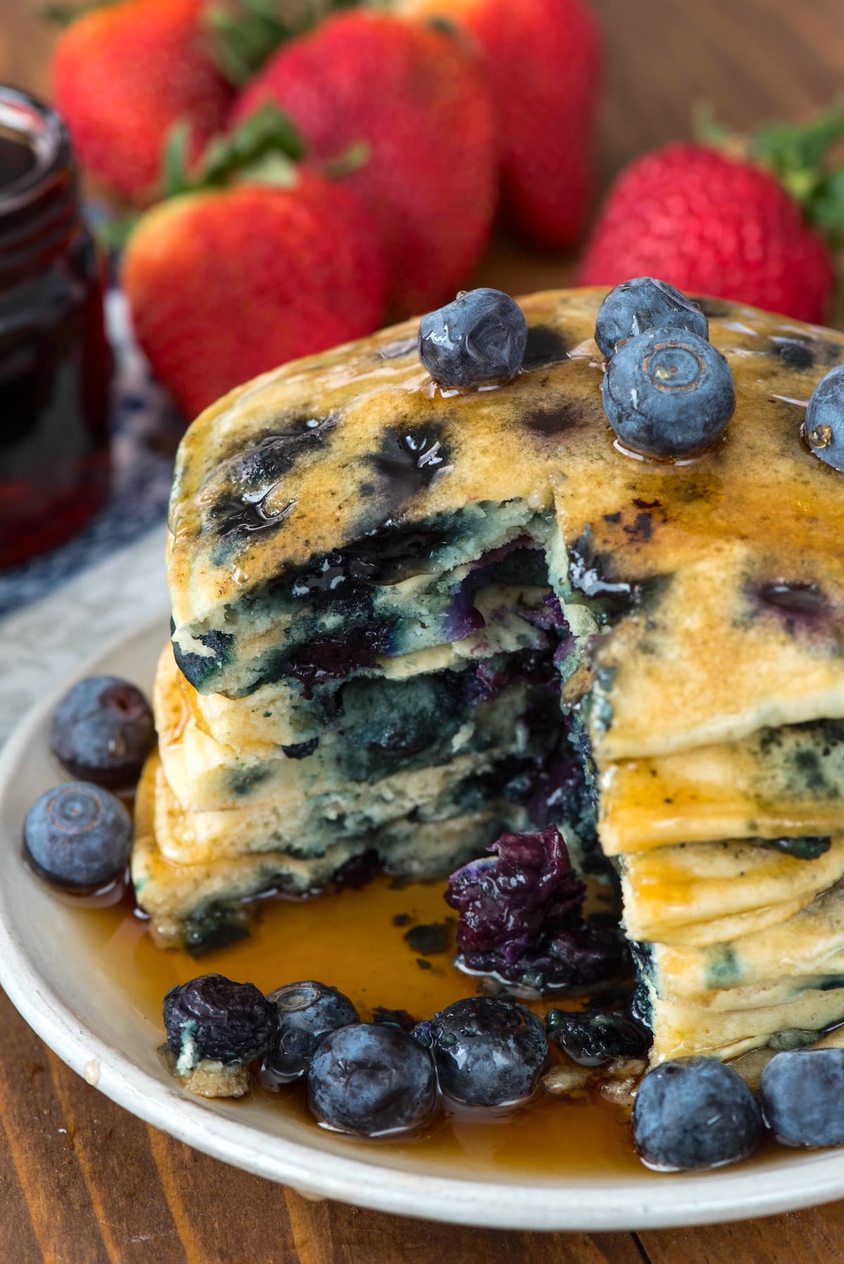 stacked pancakes with blueberries baked in and covered in syrup.