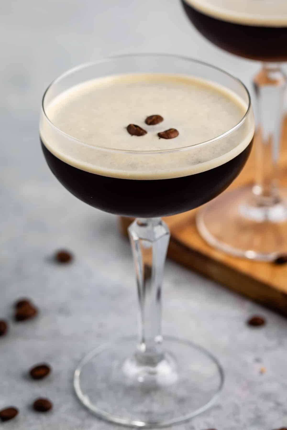 espresso martini in a tall clear glass with coffee beans all around the glass.