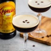 espresso martini in a tall clear glass with coffee beans all around the glass.
