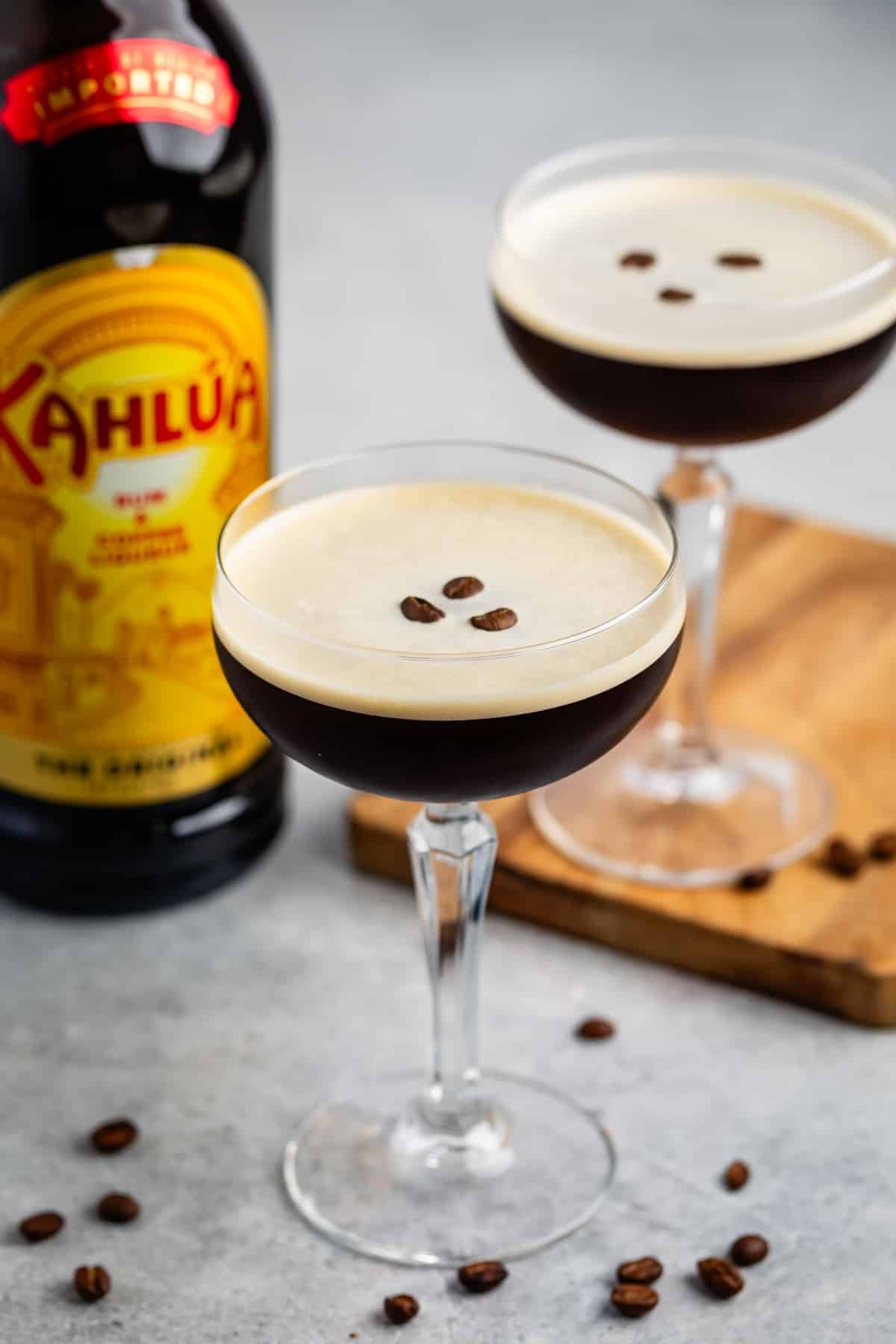 espresso martini in a tall clear glass with coffee beans all around the glass.
