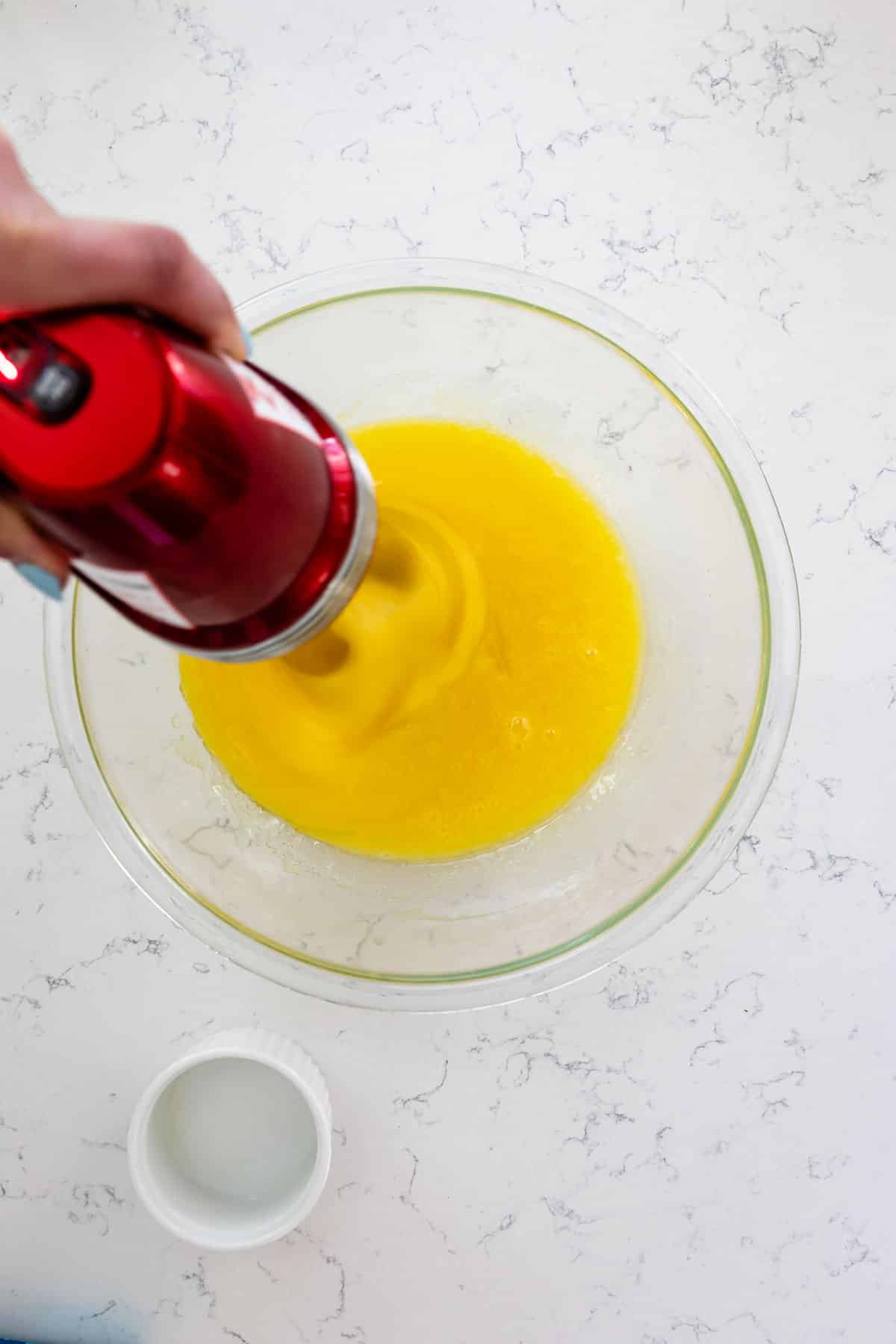 cake batter in glass bowl hand holding mixer in batter on marble background.