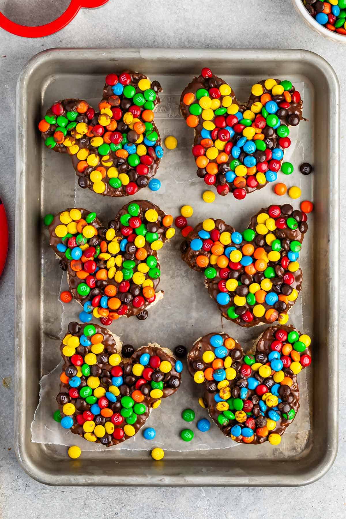 Mickey Mouse shaped Rice Krispie treats covered in chocolate and colorful M&Ms.