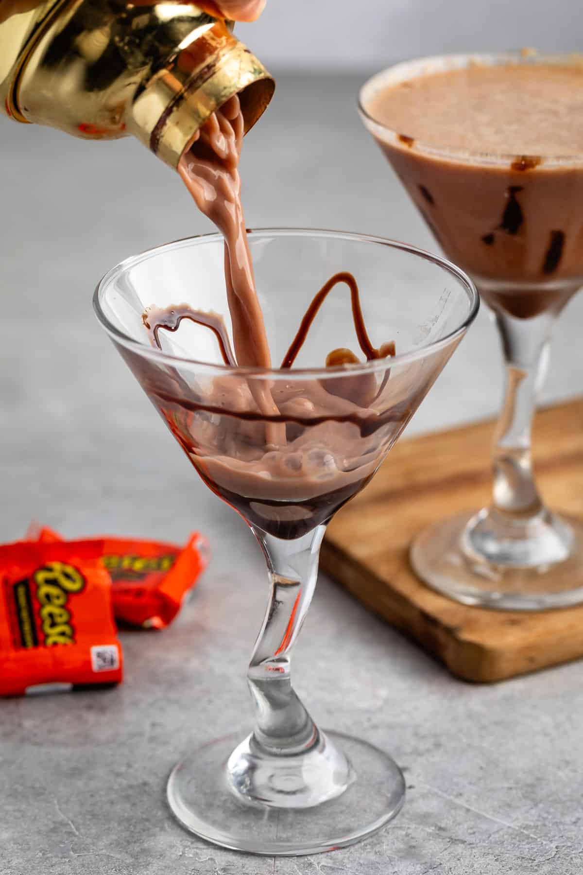 peanut butter martini in a clear tall glass with a peanut butter cup on the rim.