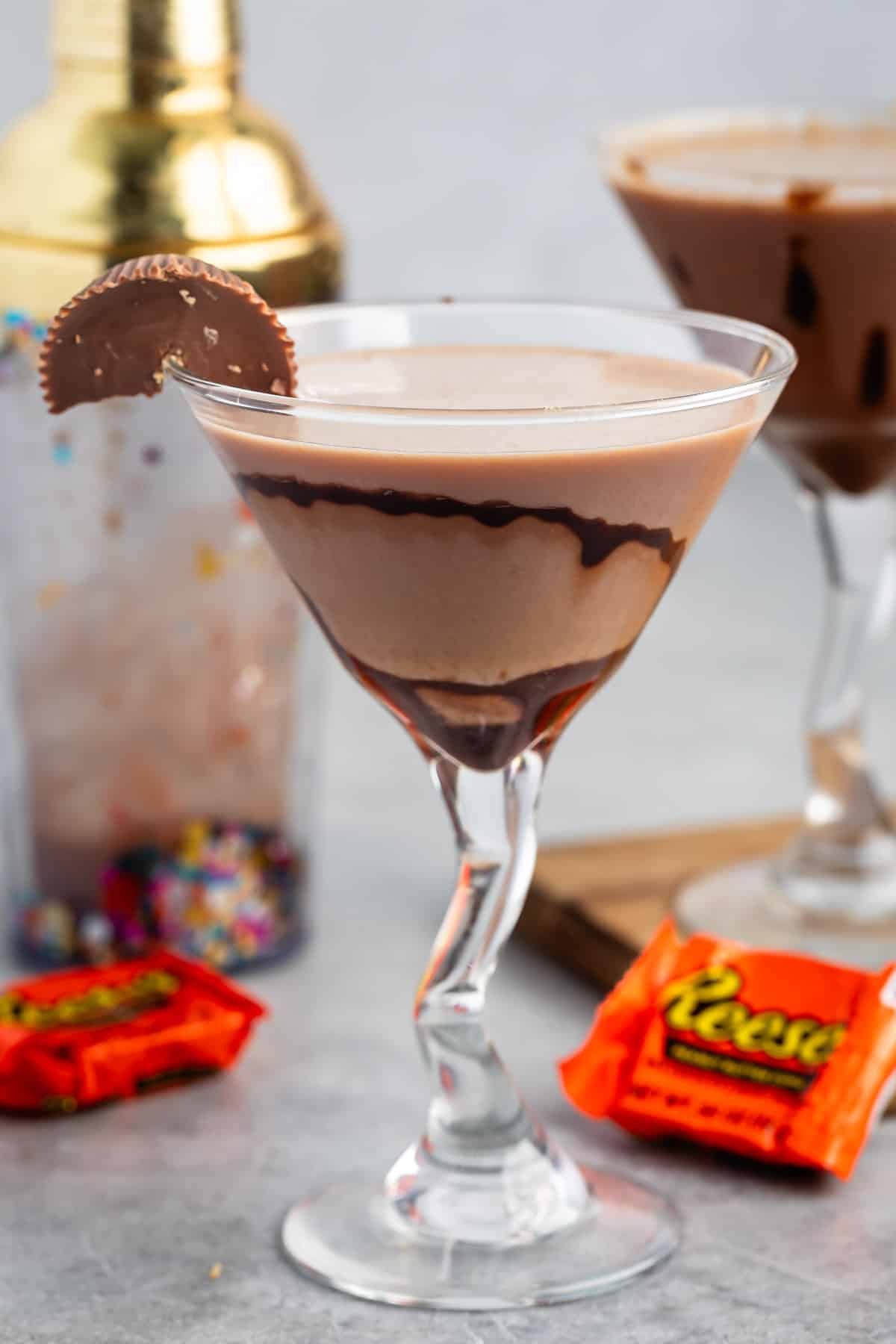 peanut butter martini in a clear tall glass with a peanut butter cup on the rim.