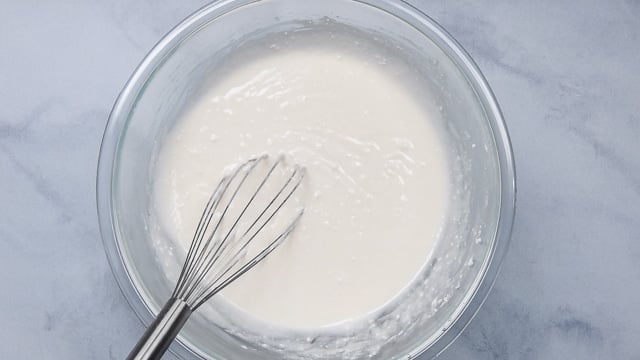 white cake batter in clear bowl with whisk