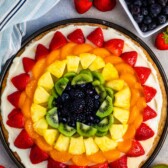 all types of fruit laid in rainbow order on a circular piece of dough.