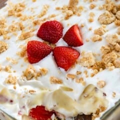 strawberry shortcake in a clear pan with sliced strawberries and crushed golden Oreos on top.