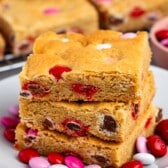 stacked blondies with pink and red and white M&Ms baked into the bars on a white plate.