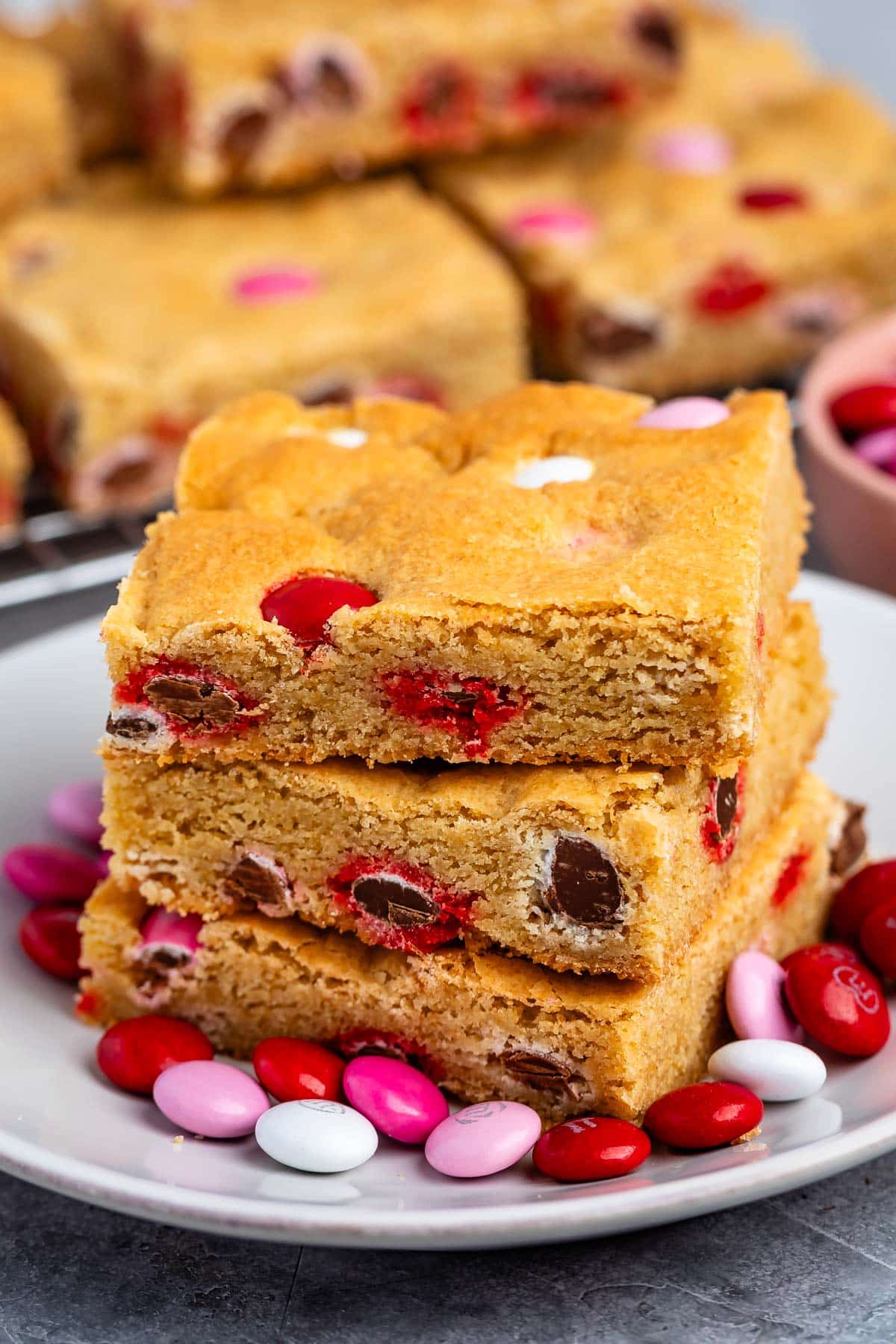 stacked blondies with pink and red and white M&Ms baked into the bars on a white plate.