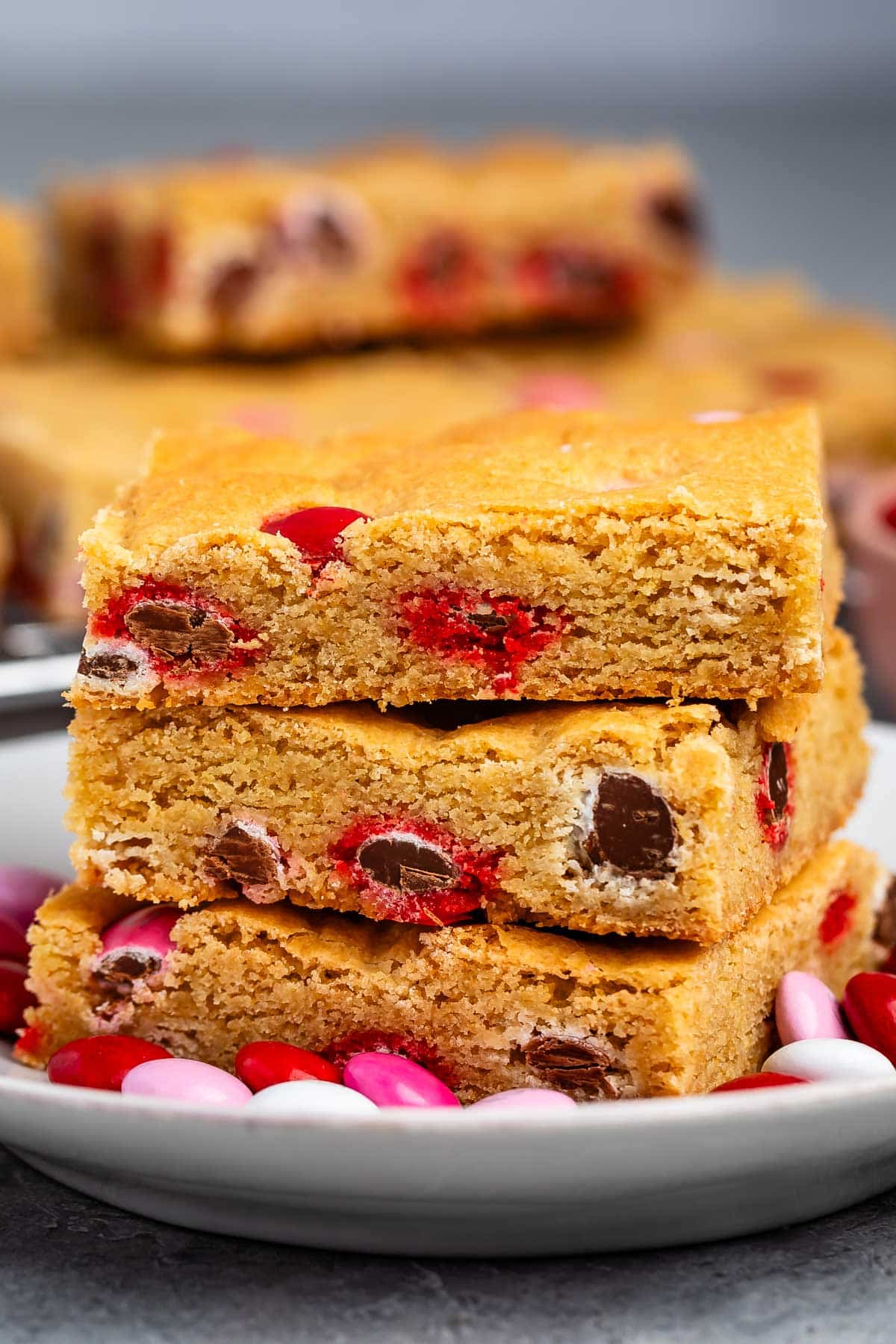 stacked blondies with pink and red and white M&Ms baked into the bars on a white plate.