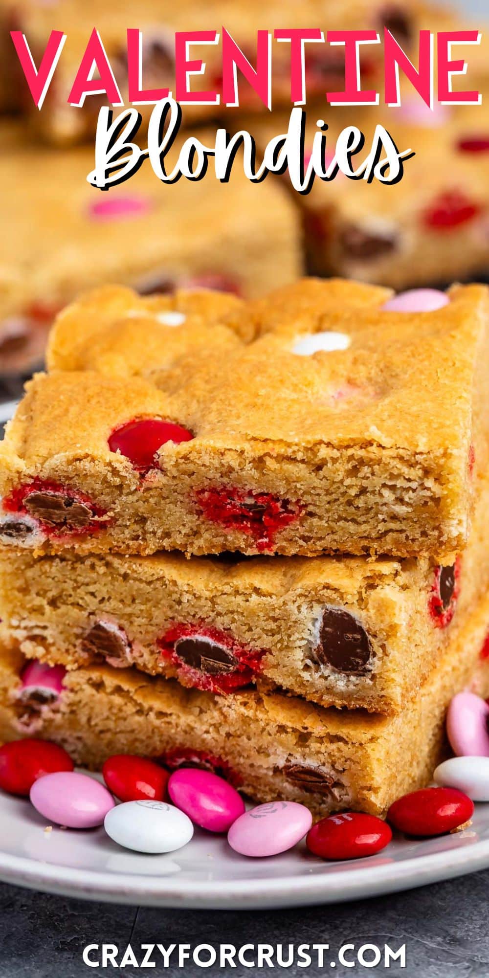 stacked blondies with pink and red and white M&Ms baked into the bars on a white plate.