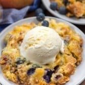 dump cake on a grey plate with blueberries mixed in and a scoop of ice cream on top.