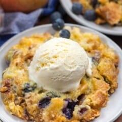 dump cake on a grey plate with blueberries mixed in and a scoop of ice cream on top.