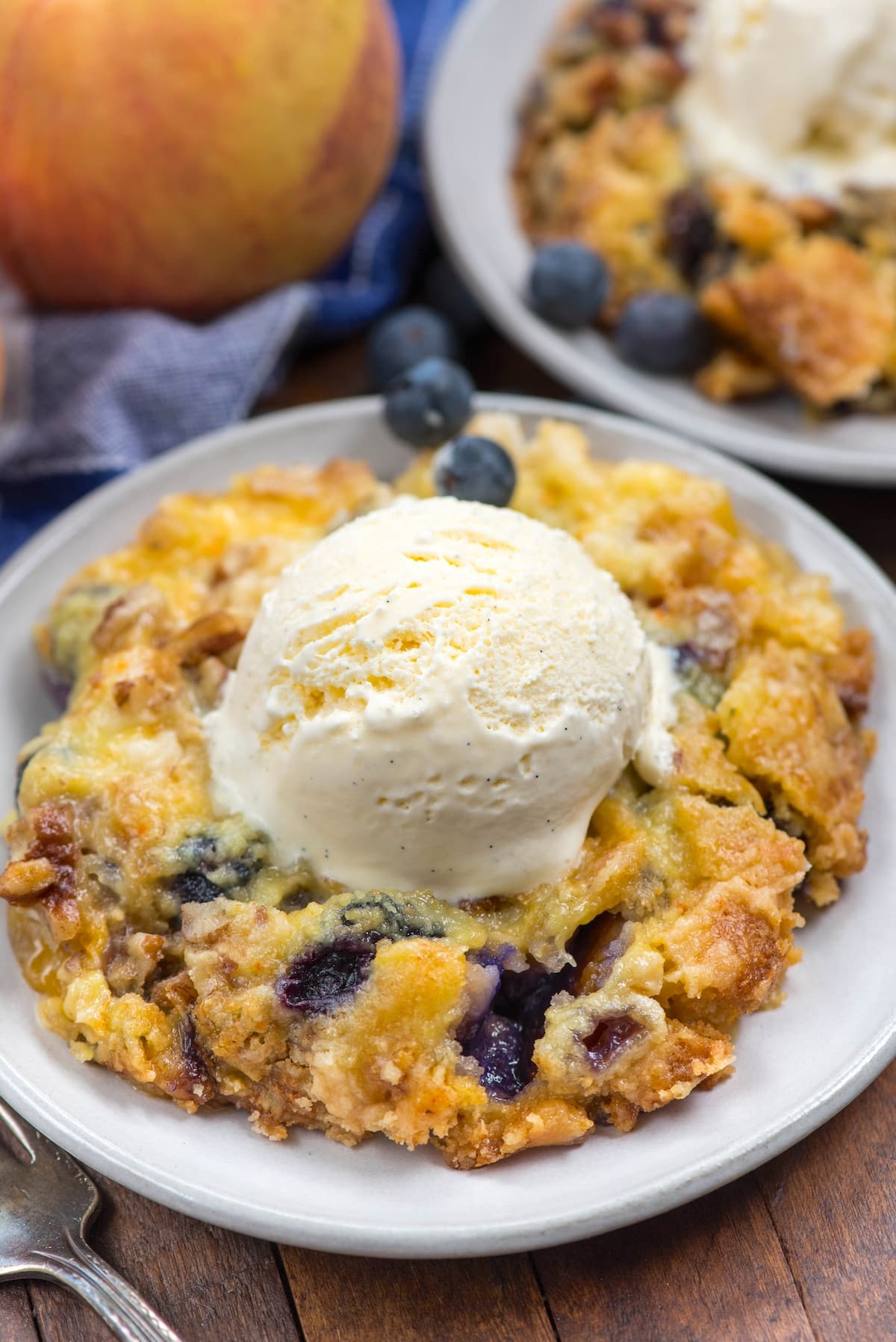 dump cake on a grey plate with blueberries mixed in and a scoop of ice cream on top.