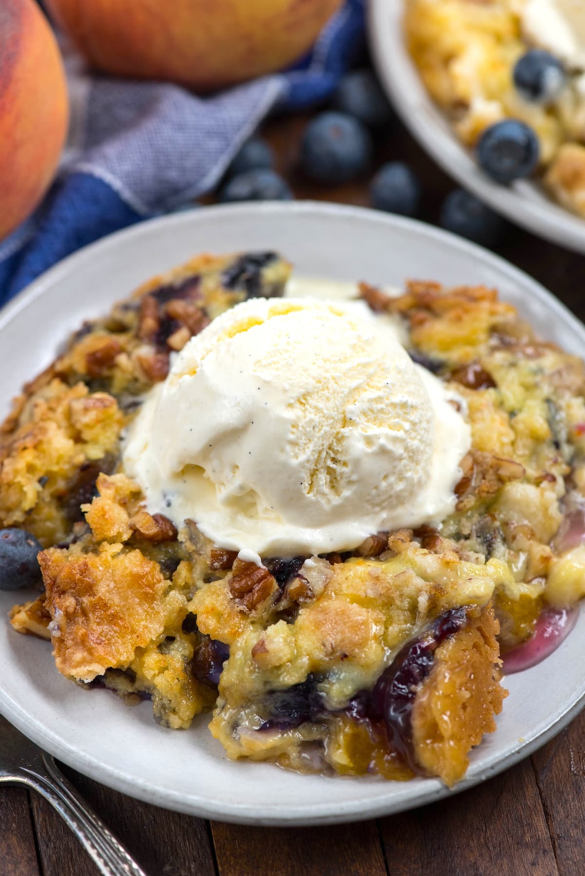 dump cake on a grey plate with blueberries mixed in and a scoop of ice cream on top.