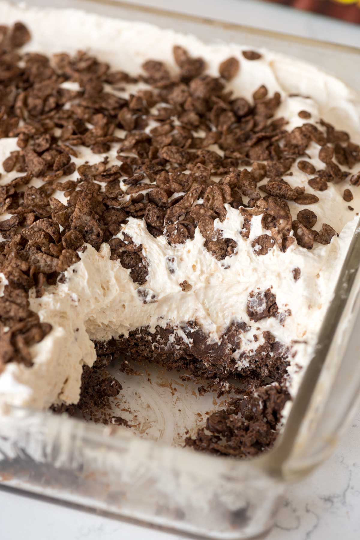 cocoa pebble dessert layered with chocolate and cream in a clear pan.