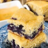 stacked cornbread on a blue and white plate surrounded by blueberries.