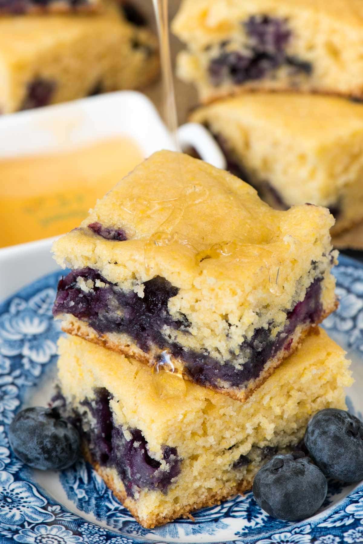 stacked cornbread on a blue and white plate surrounded by blueberries.