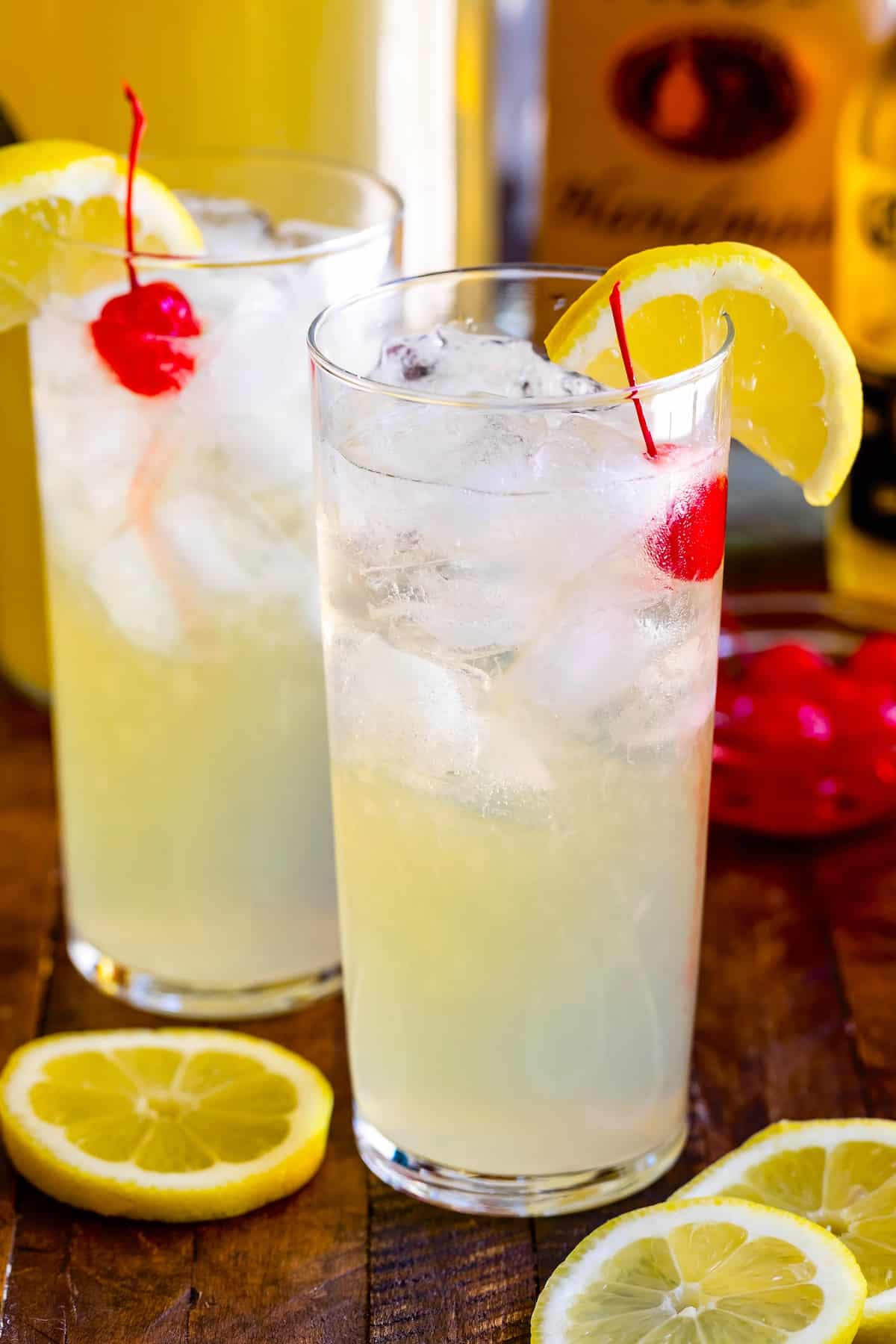 yellow party punch in a tall clear class with a cherry and lemon slice on the rim.