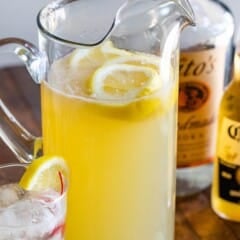 yellow party punch in a tall clear pitcher with lemon slices inside.