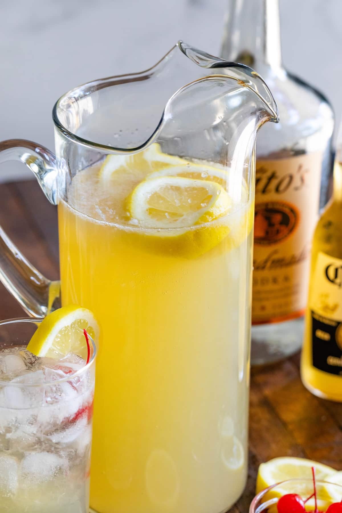 yellow party punch in a tall clear pitcher with lemon slices inside.