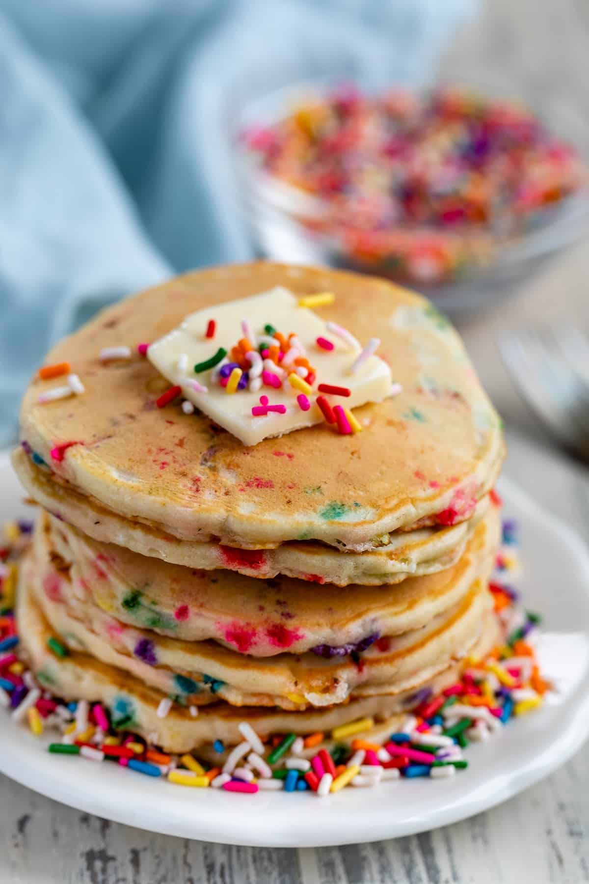 stacked sprinkle pancakes with colorful sprinkles all around and baked in with butter on top.
