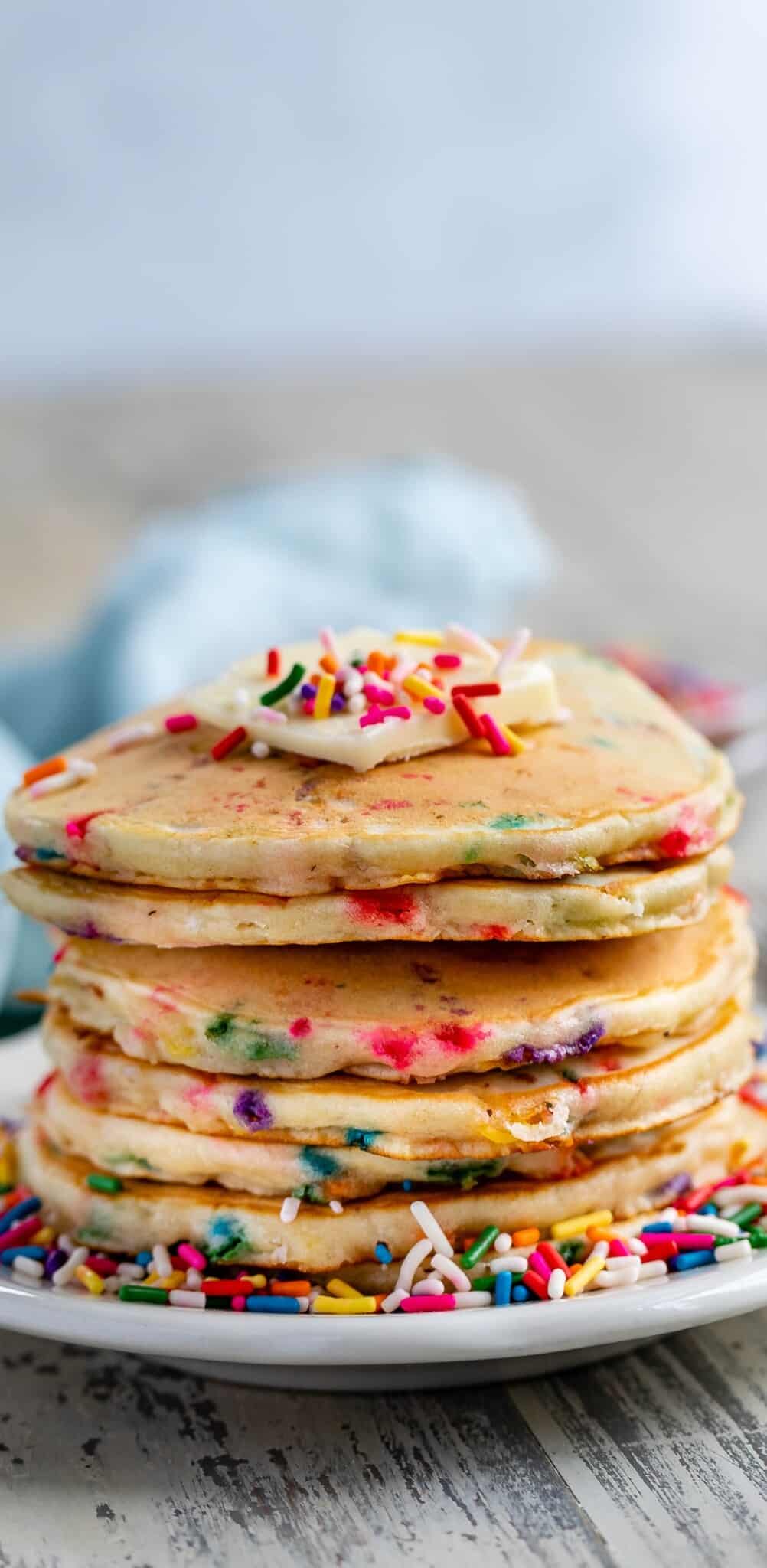 stacked sprinkle pancakes with colorful sprinkles all around and baked in with butter on top.