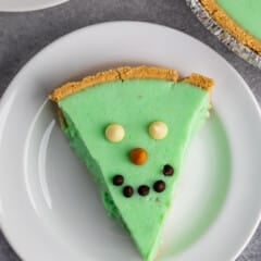 green alligator pie with chocolate chips on top making it a face on a white plate.