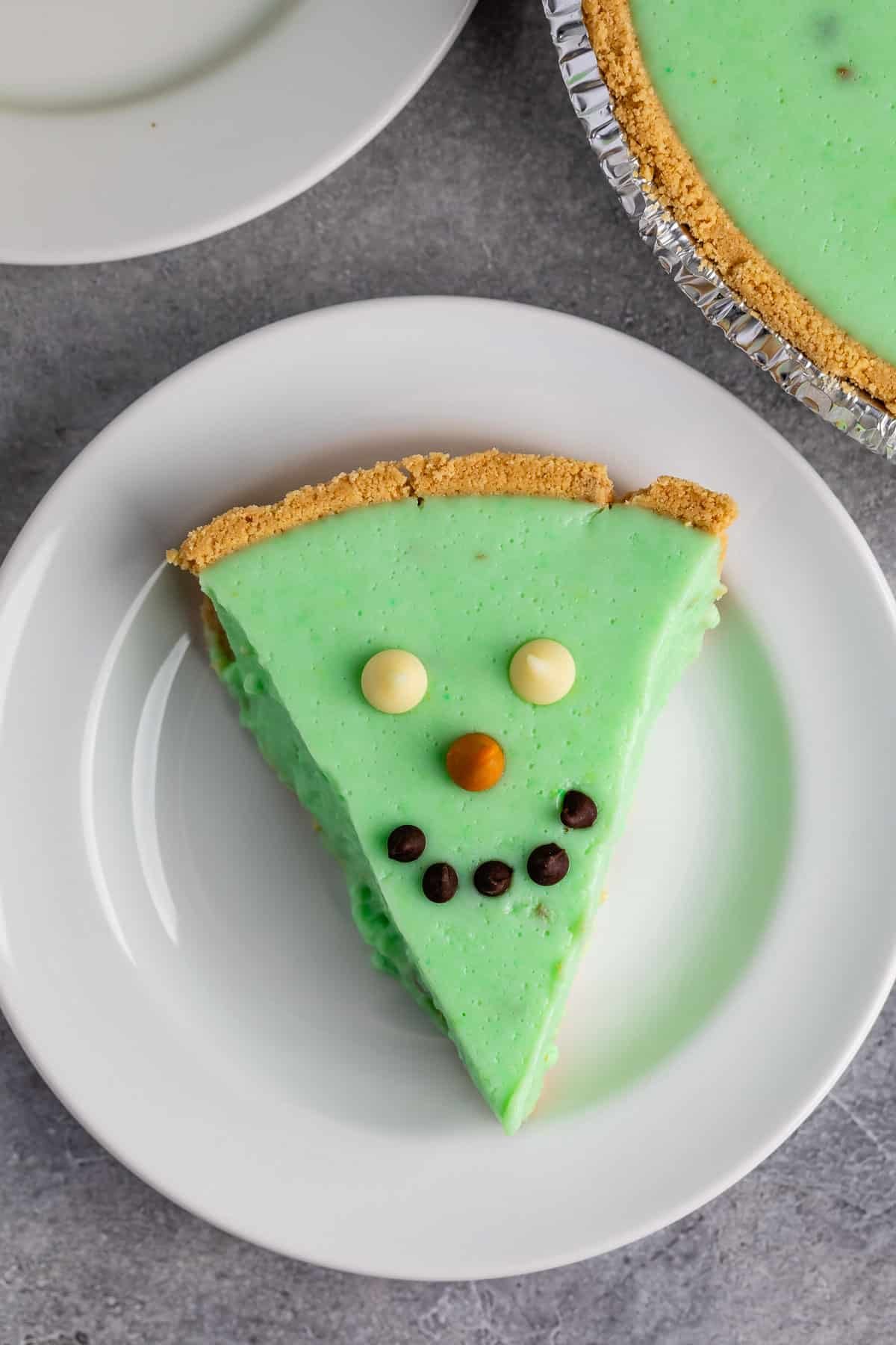 green alligator pie with chocolate chips on top making it a face on a white plate.