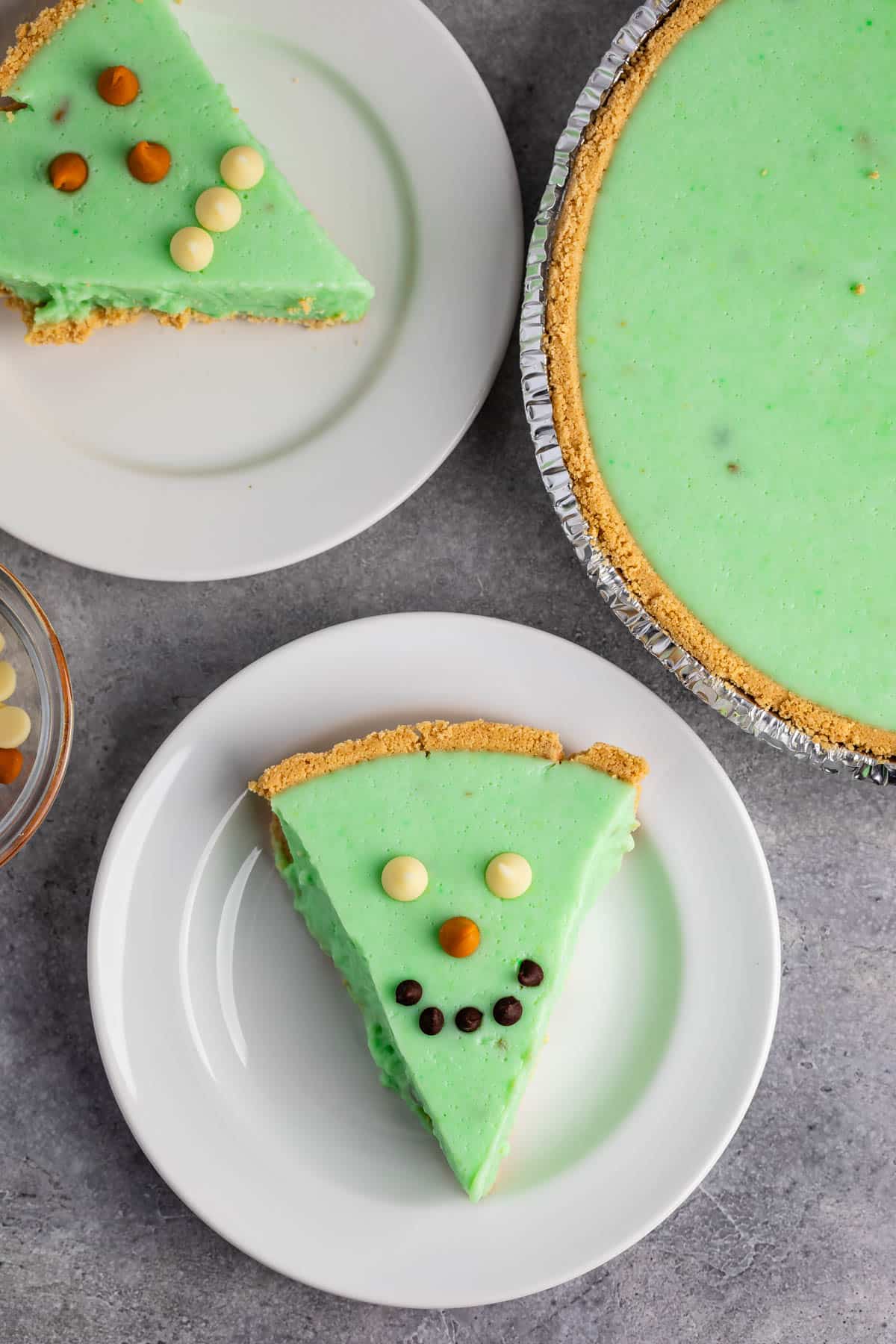 green alligator pie with chocolate chips on top making it a face on a white plate.