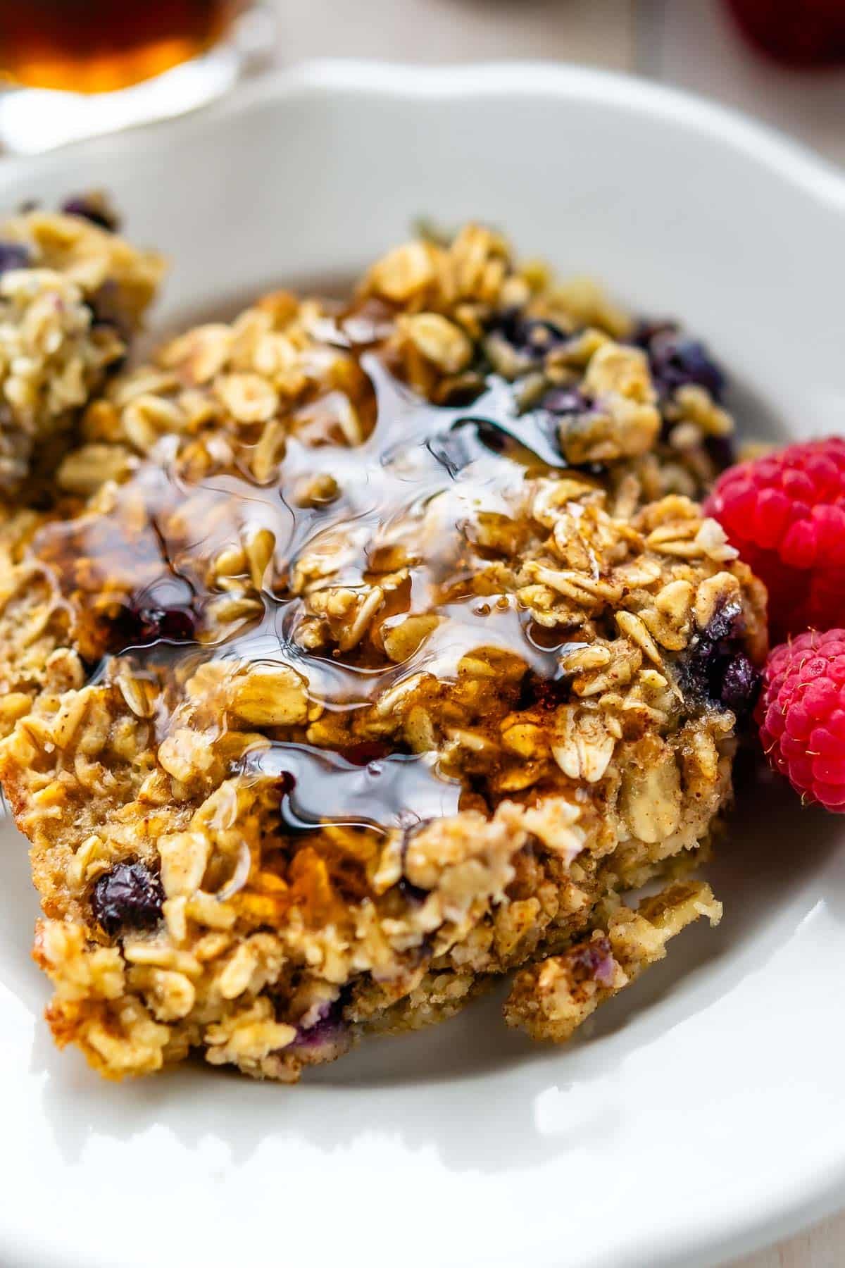 oatmeal in a white plate next to raspberries.