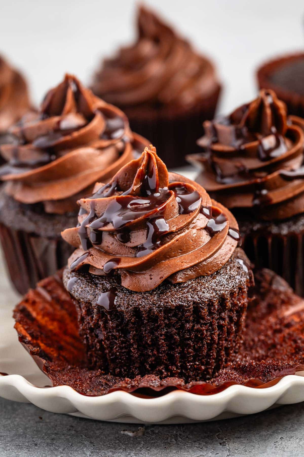 unwrapped cupcake with chocolate frosting and chocolate sauce drizzled over top.