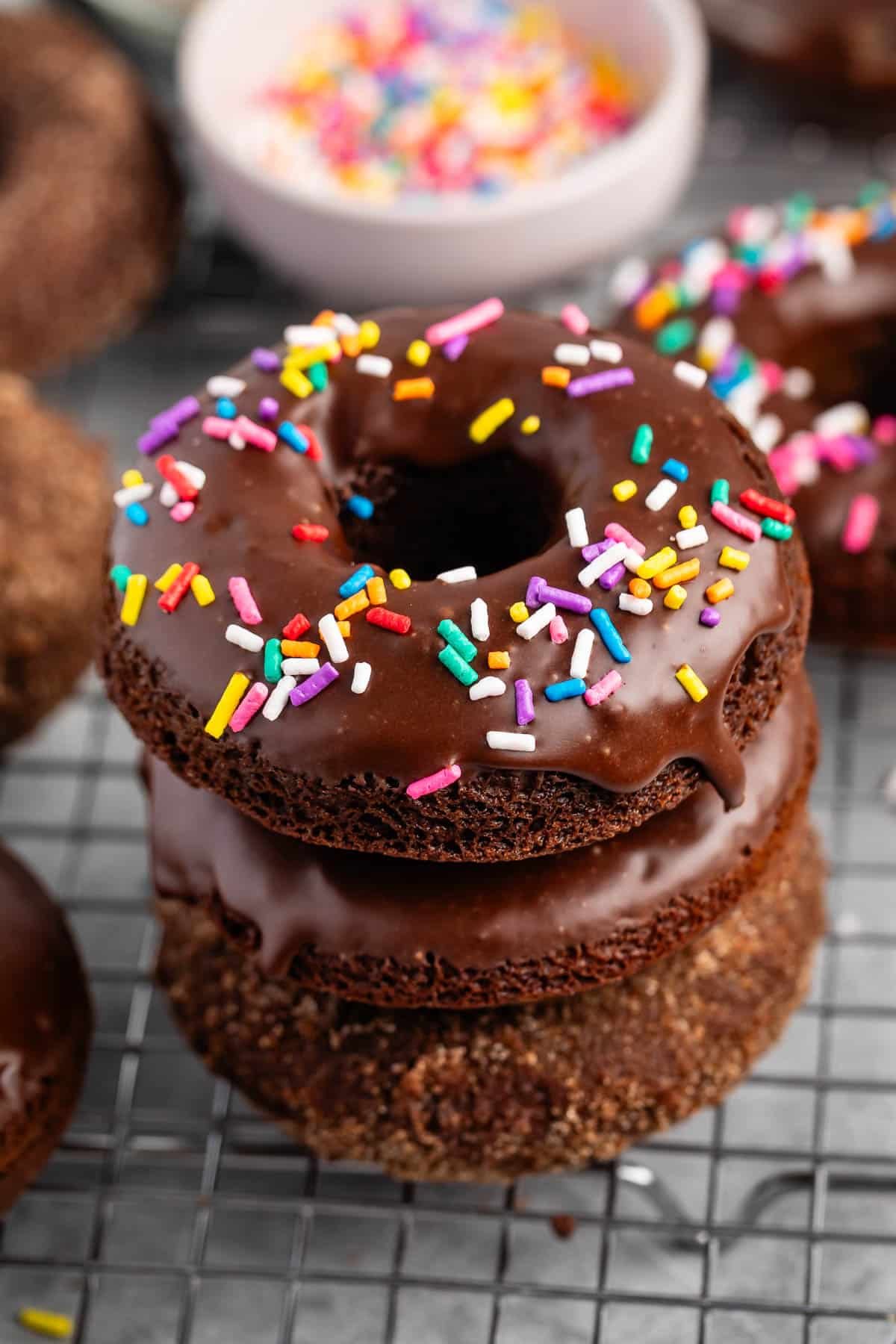 stacked chocolate donuts with chocolate glaze and colorful sprinkles on top,