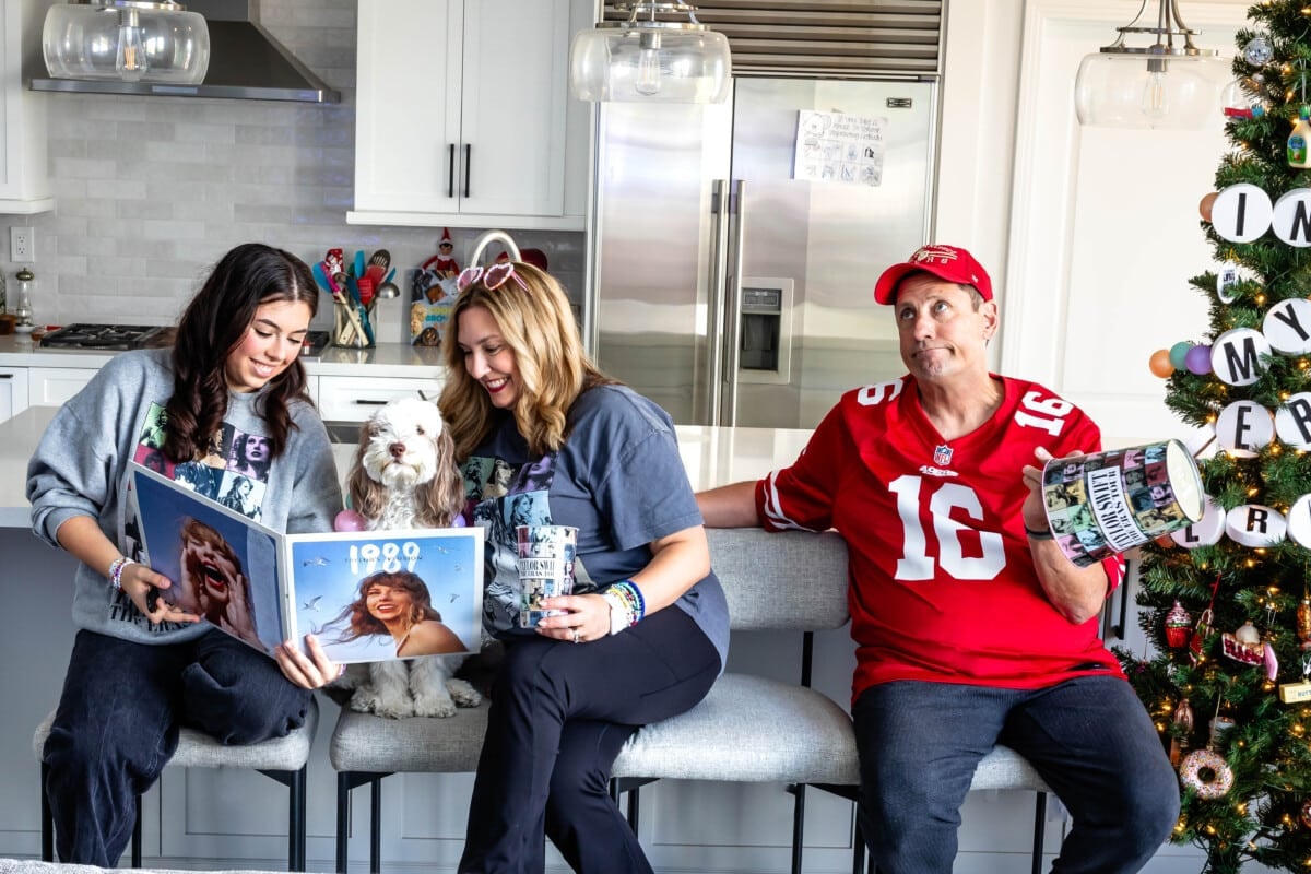mom and daughter and dad sitting at a kitchen island. Mom and daughter are wearing Taylor Swift merchandise holing a record. Dad is wearing a 49ers jersey and hat.