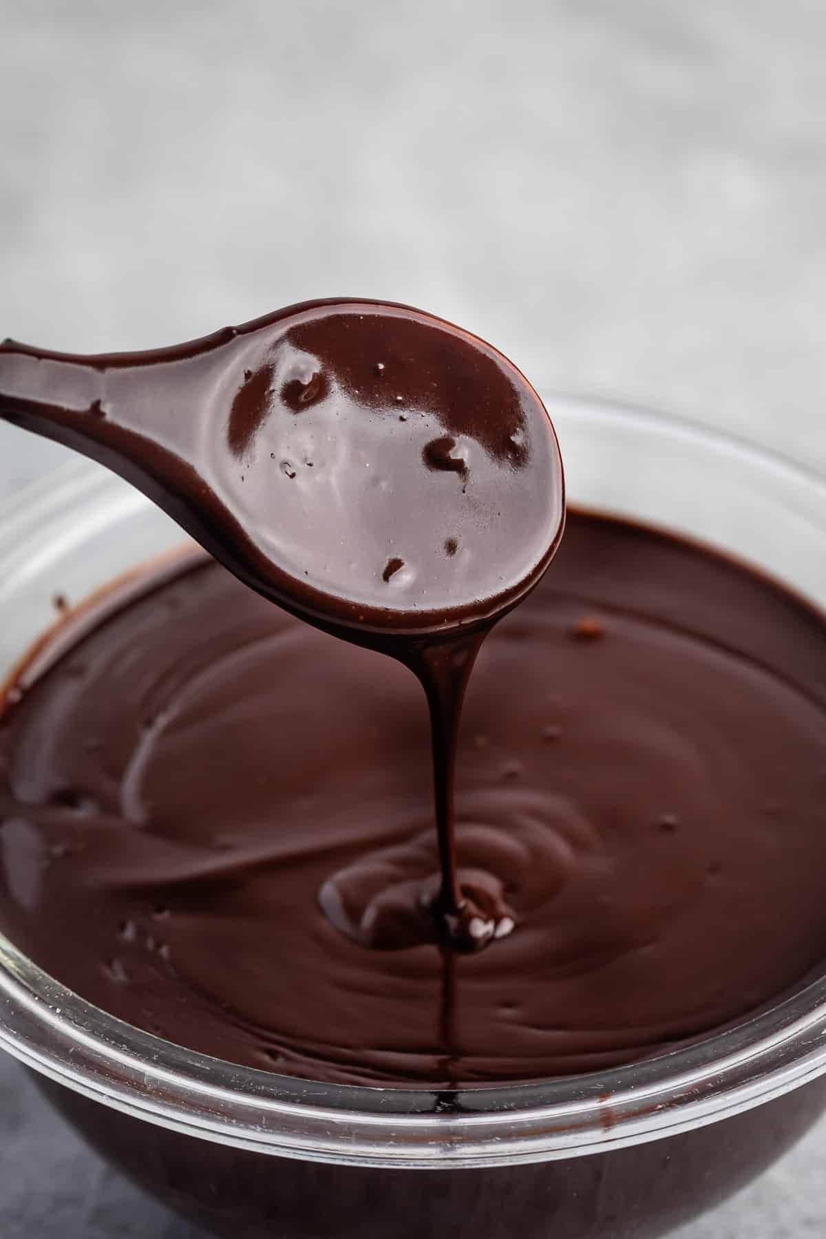 chocolate being swirled in a clear bowl with a wooden spoon.