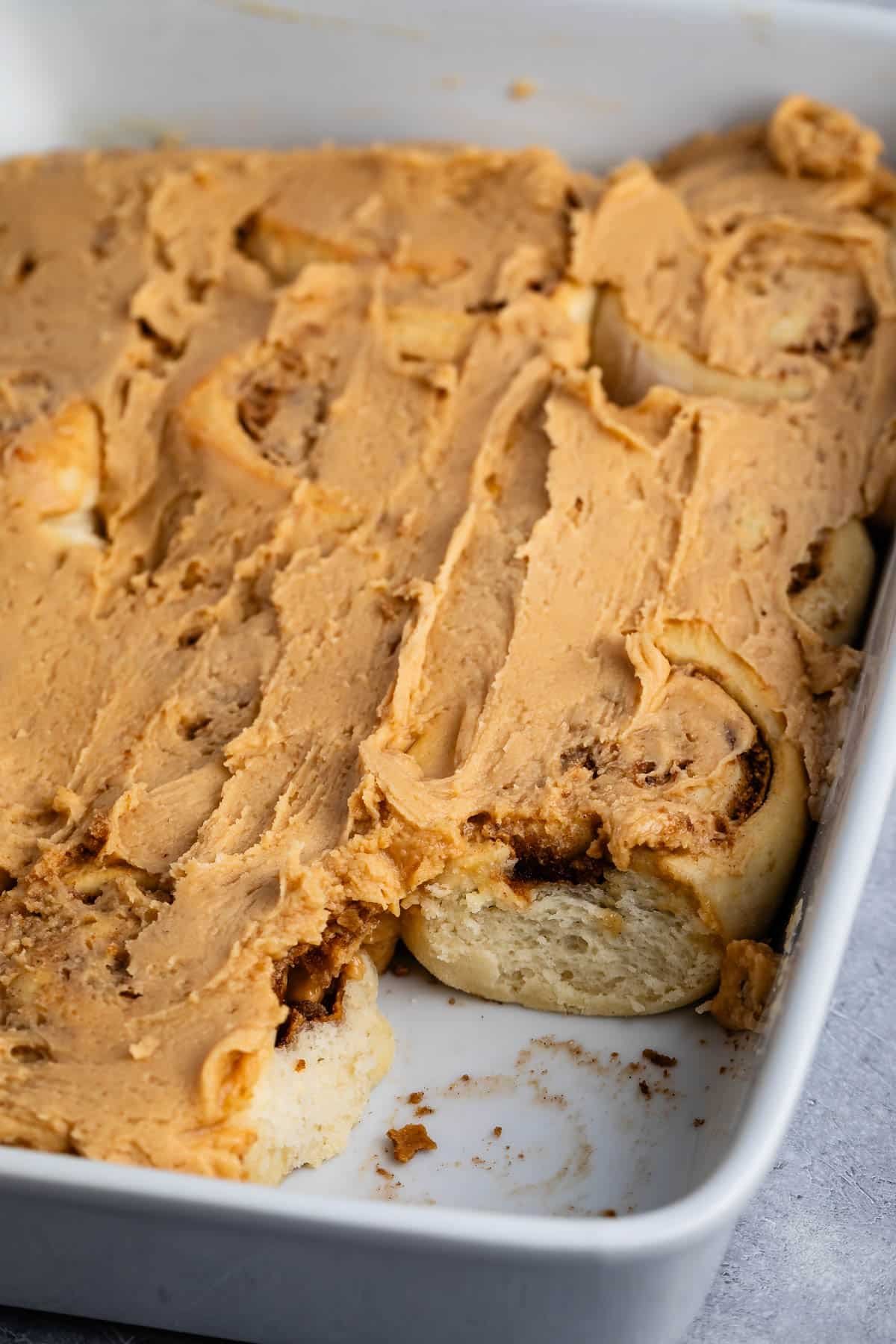 peanut butter cinnamon rolls in a white glass pan covered in peanut butter frosting.