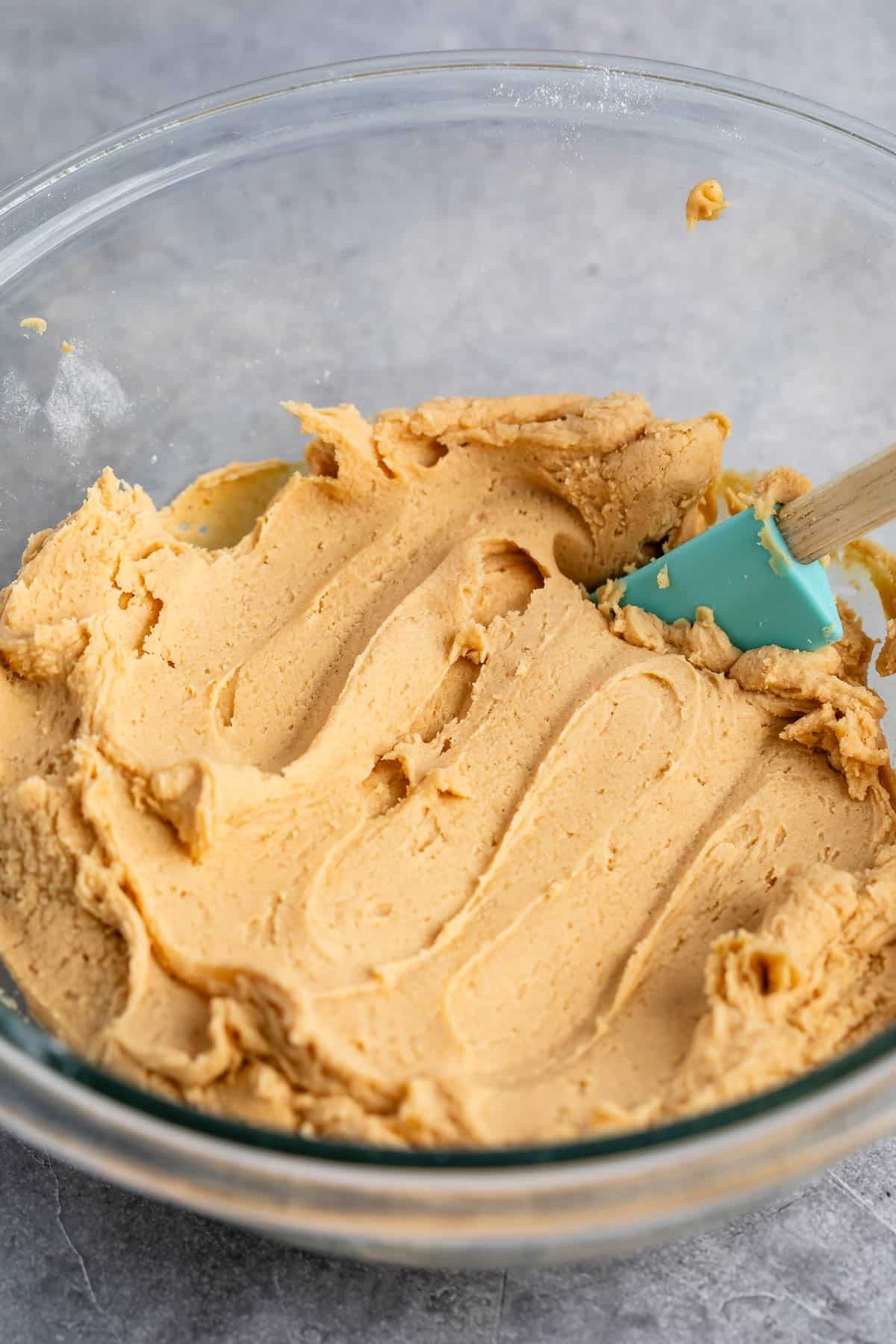 peanut butter frosting in a clear bowl with a teal spatula.