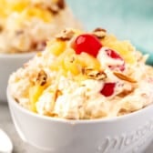 pineapple fluff with nuts and cherries on top in a white bowl.