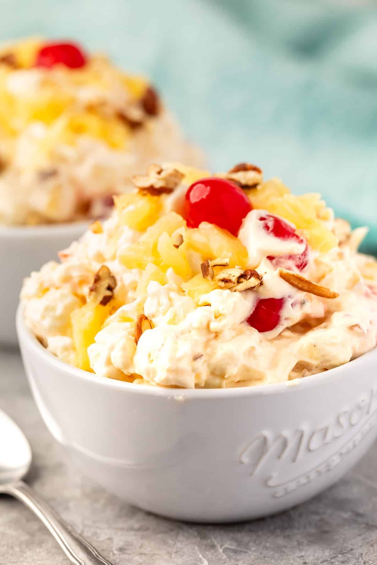 pineapple fluff with nuts and cherries on top in a white bowl.