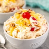 pineapple fluff with nuts and cherries on top in a white bowl.