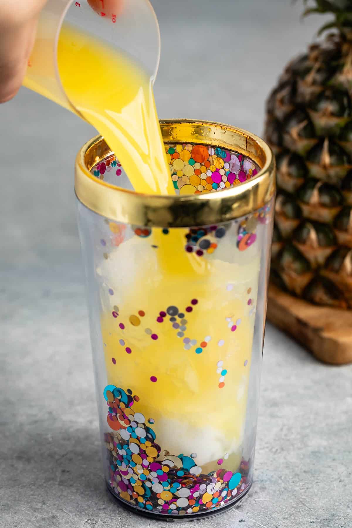 hand pouring the yellow drink into a tall drink shaker.