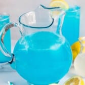 big glass pitcher filled with a bright blue drink and lemon sliced all around.