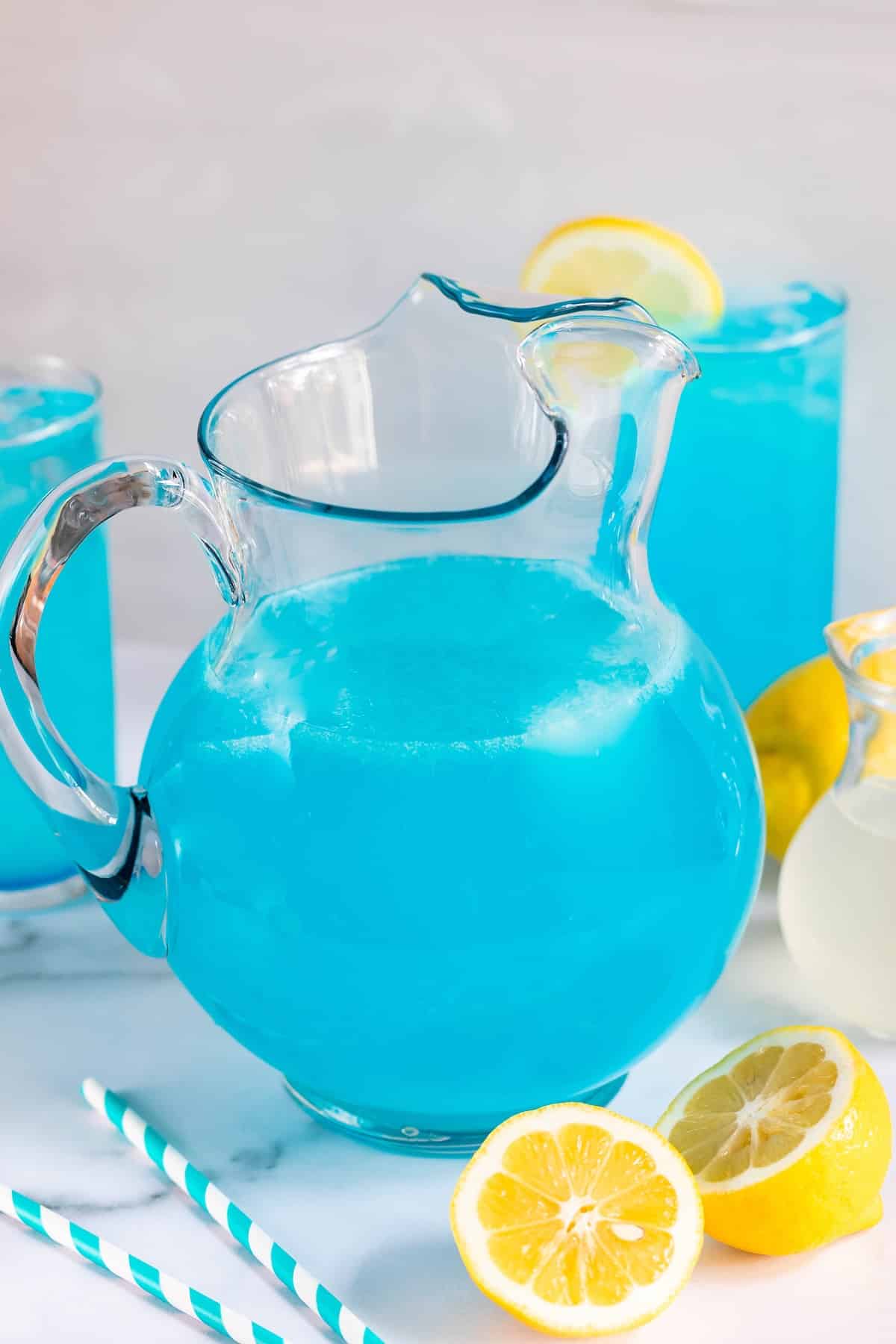 big glass pitcher filled with a bright blue drink and lemon sliced all around.