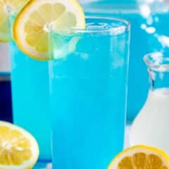 tall clear glass with a bright blue drink inside and a lemon slice on the rim.