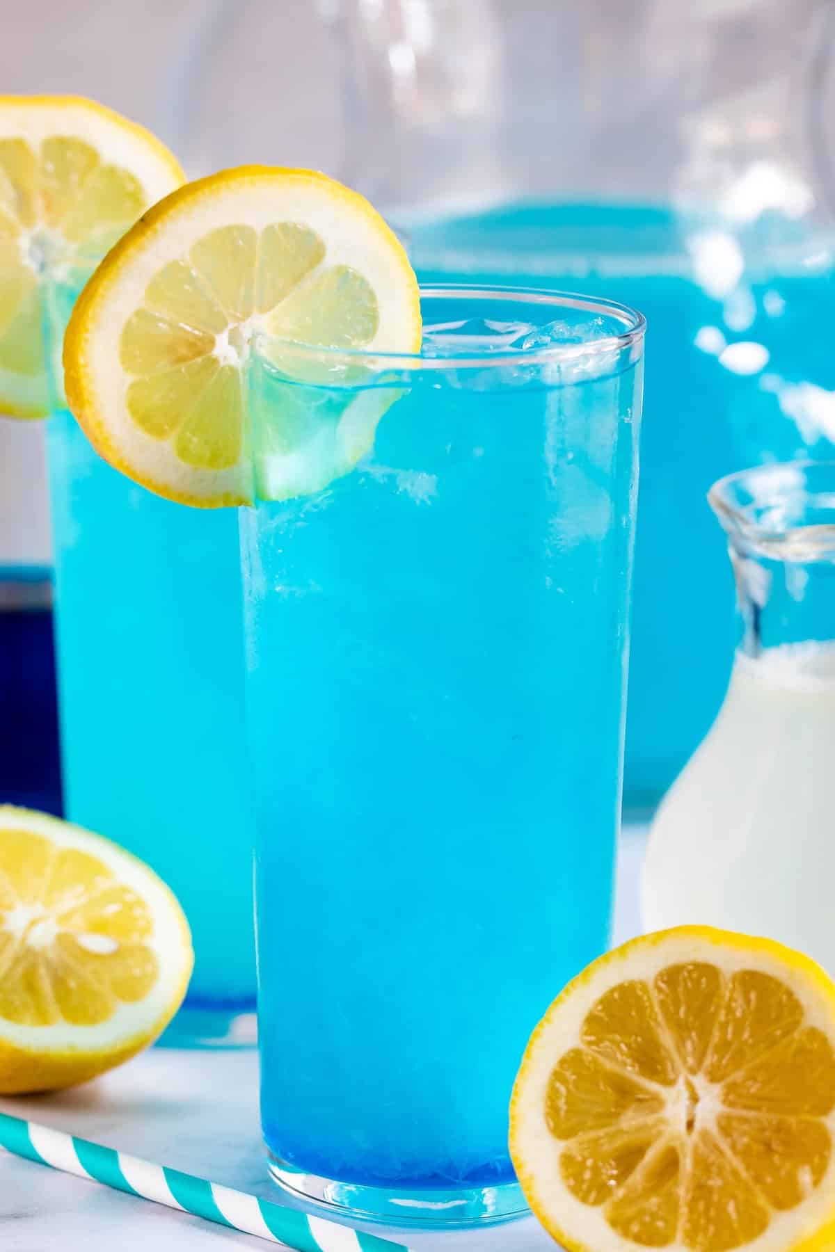 tall clear glass with a bright blue drink inside and a lemon slice on the rim.