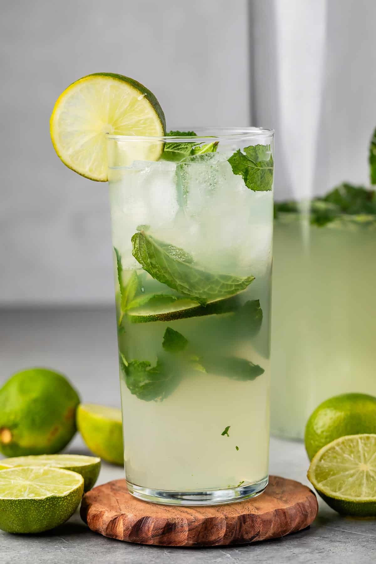 mojito in a tall clear glass with sliced limes in and around the glass with mint.