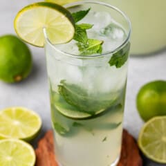 mojito in a tall clear glass with sliced limes in and around the glass with mint.