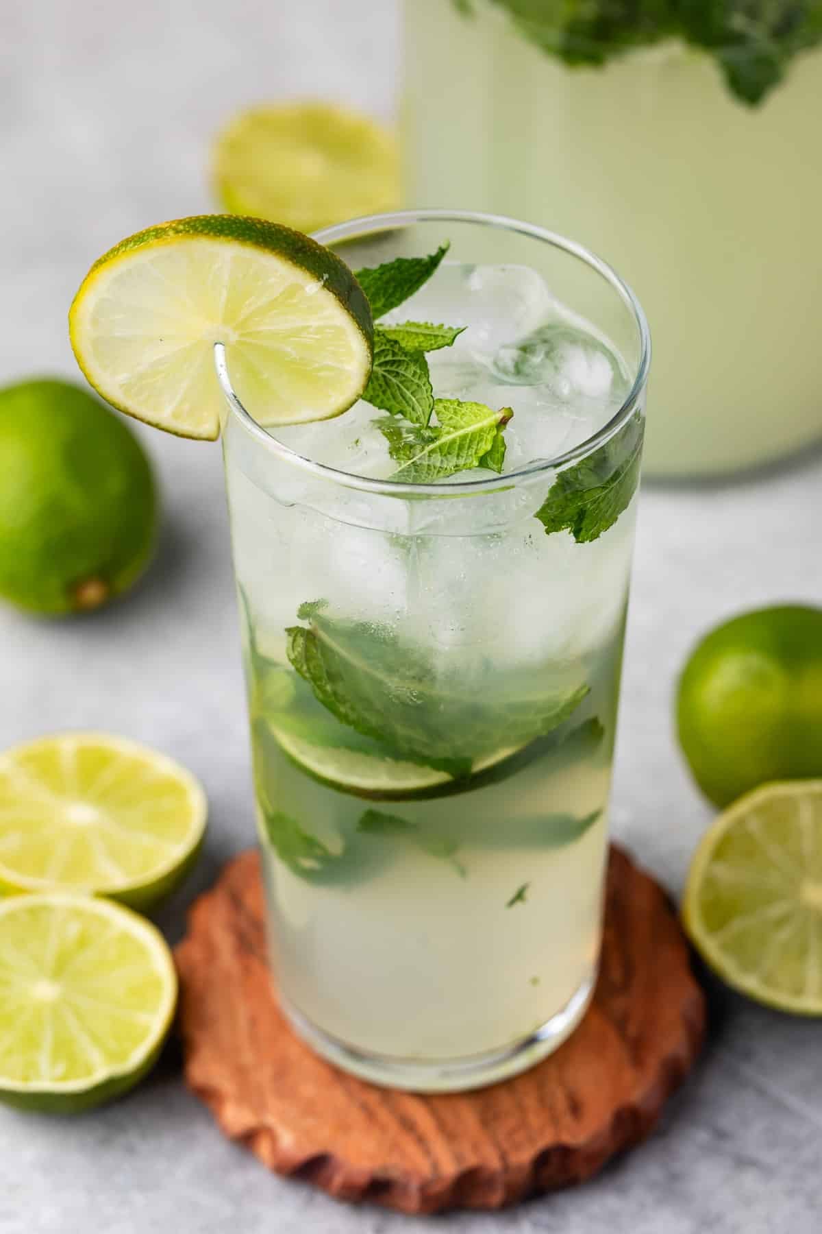 mojito in a tall clear glass with sliced limes in and around the glass with mint.