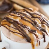 cheesecake dip in a white mug with caramel and chocolate drizzled over top.