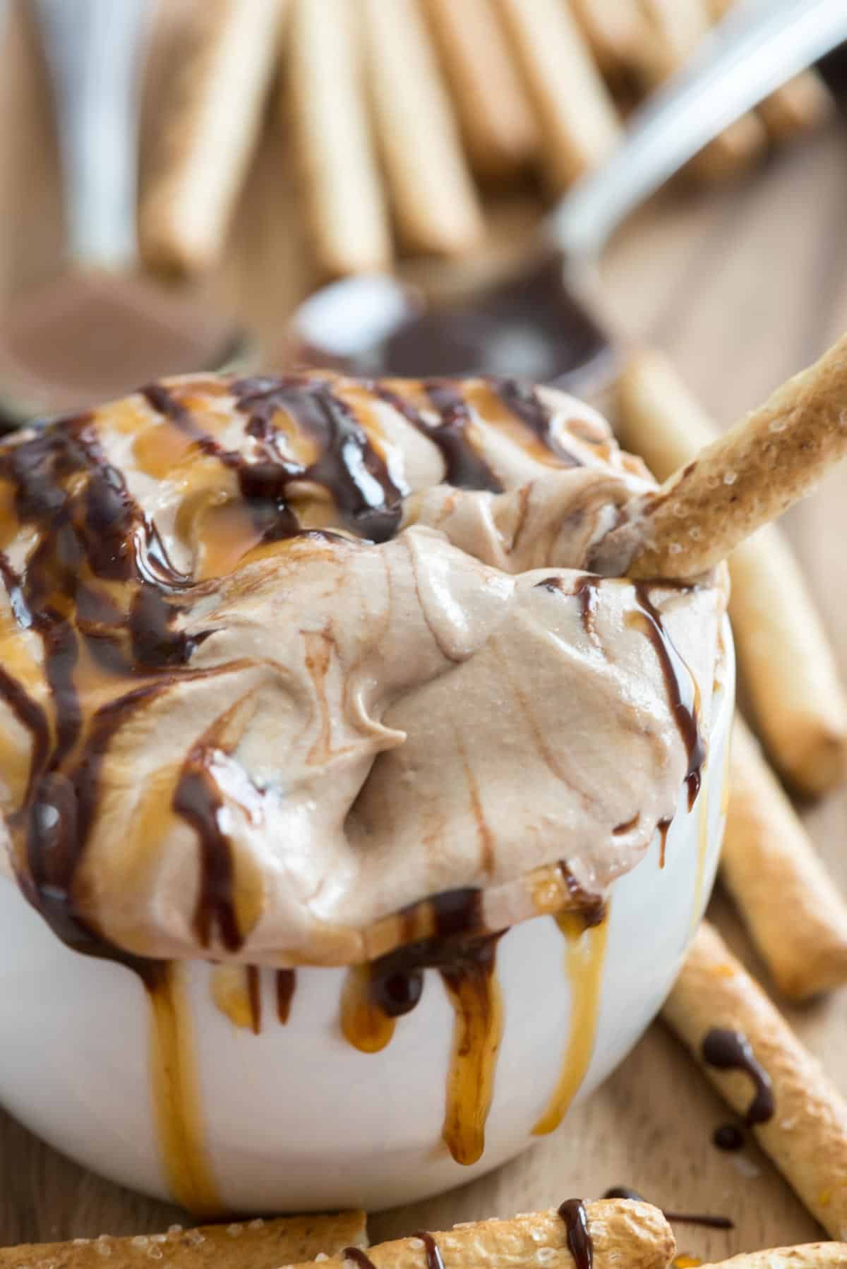 cheesecake dip in a white mug with caramel and chocolate drizzled over top.